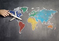 Top view of crop anonymous person holding toy airplane on colorful world map drawn on chalkboard
